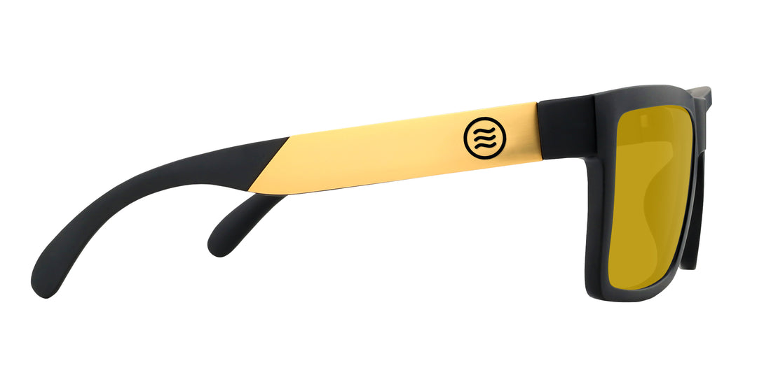 Close side view of Prospector XL sunglasses showing black matte frame, gold metal temple with logo, and yellow lenses on white background