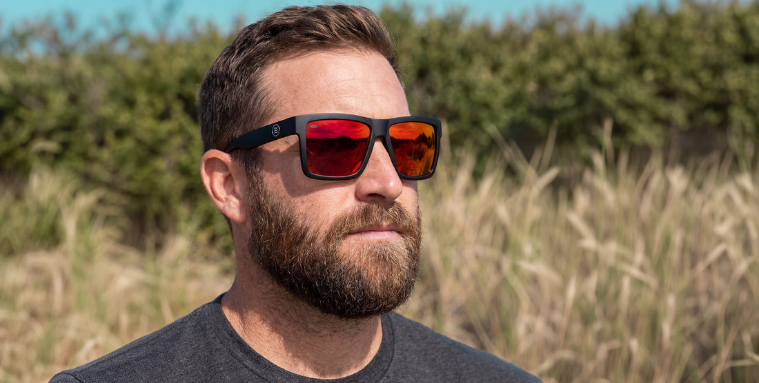 Man wearing matte black Supernova XL sunglasses with red mirrored polarized lenses in coastal dune grasses