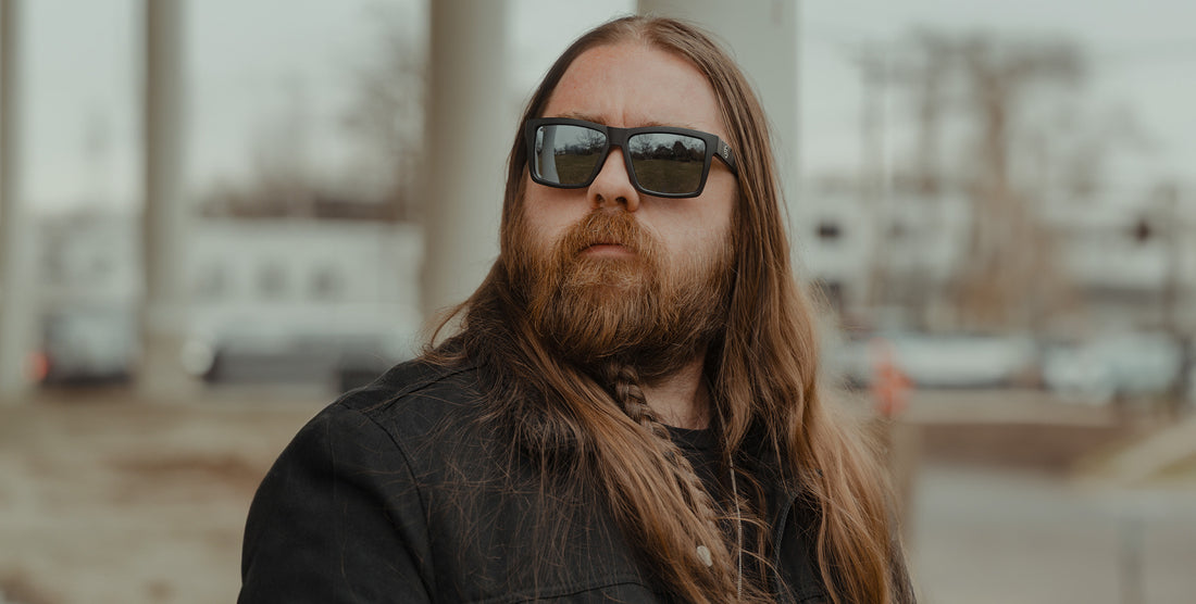 Bearded man wearing Ace black rectangular sunglasses outdoors with a blurred urban background