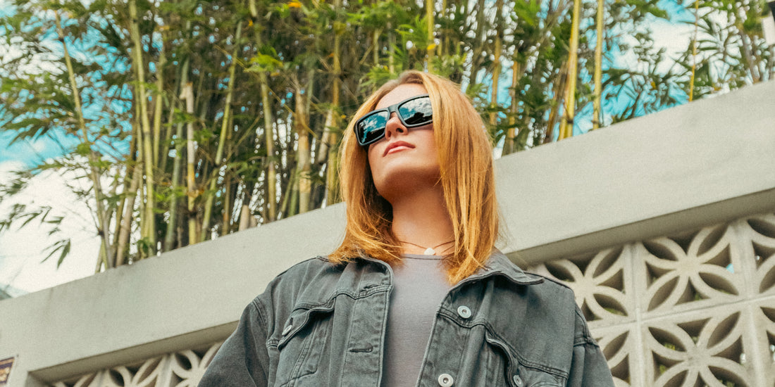 Woman wearing black Lowrider polarized sunglasses outdoors in front of bamboo and a patterned concrete wall