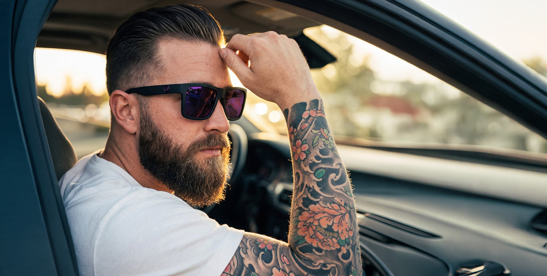 Tattooed man wearing Nightshade sunglasses while seated in a car at sunset, matte black frame and purple polarized lenses