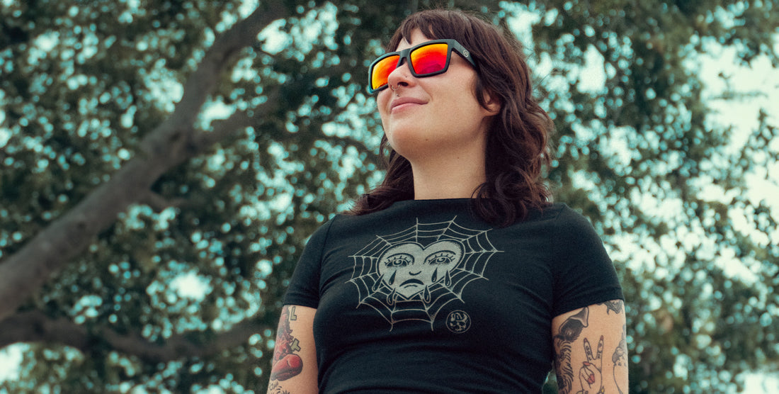 Person wearing black Supernova sunglasses with red mirrored polarized lenses looking up outdoors against trees