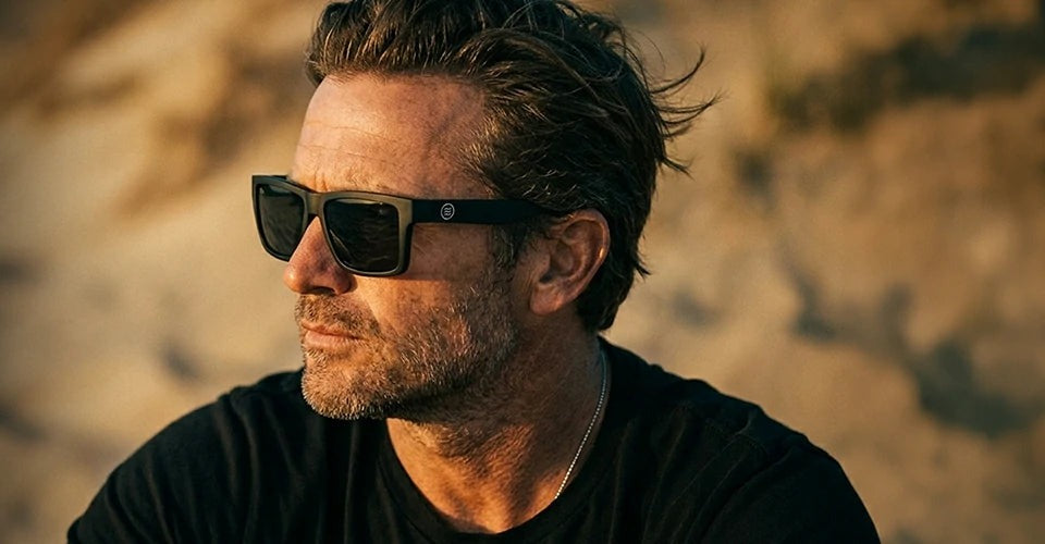 A man on a sunlit desert hillside wearing dark Neven frames.